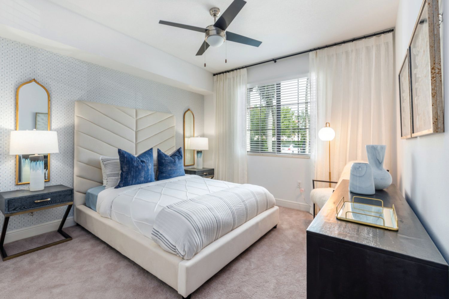 Modern bedroom with a white bed, blue pillows, lamps, and minimal decor.