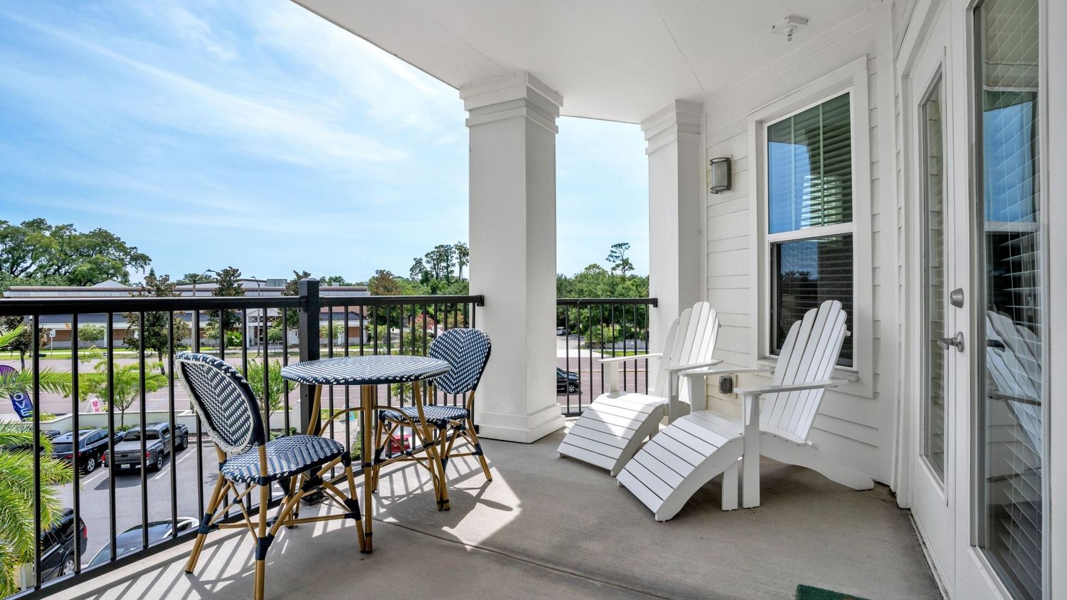 A light-filled balcony with two chairs and a small table, overlooking a lush view.