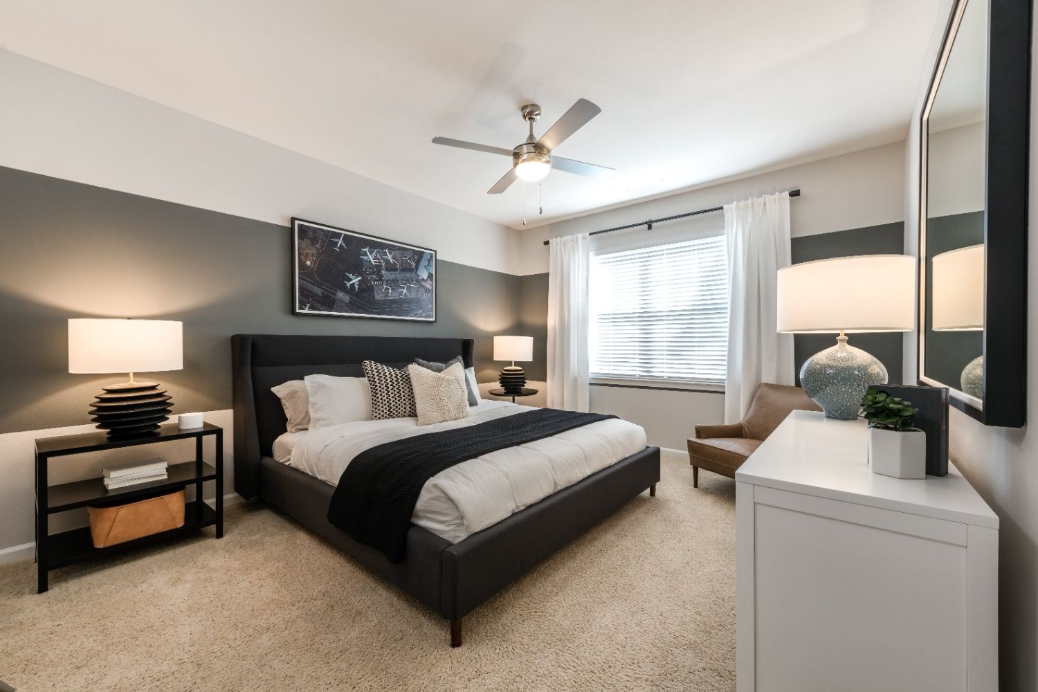 Modern bedroom with a bed, lamps, a mirror, and a window.