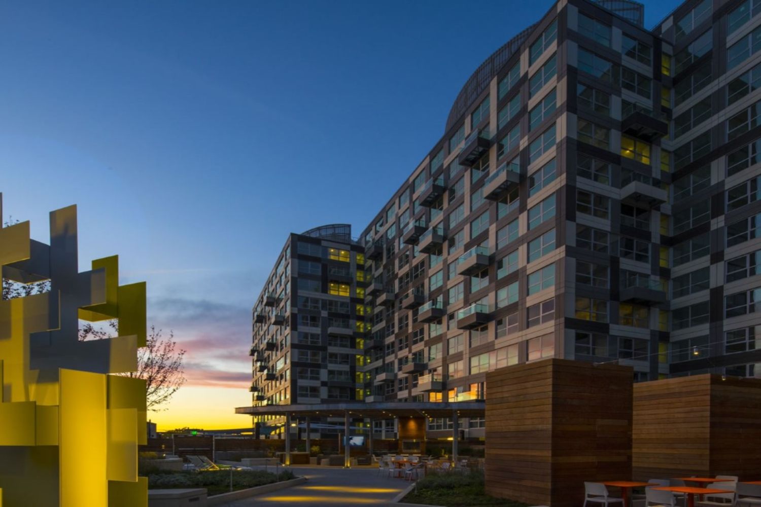 Modern apartment building at sunset with geometric yellow sculpture in the foreground.