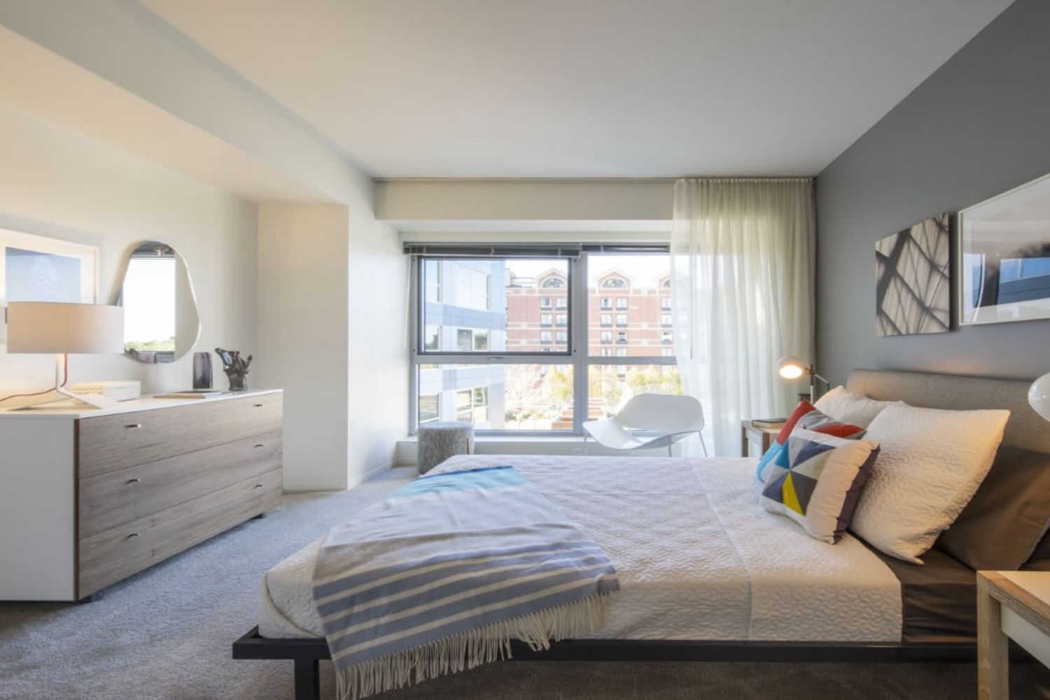 Modern bedroom with a bed, window, dresser, and minimalist decor.