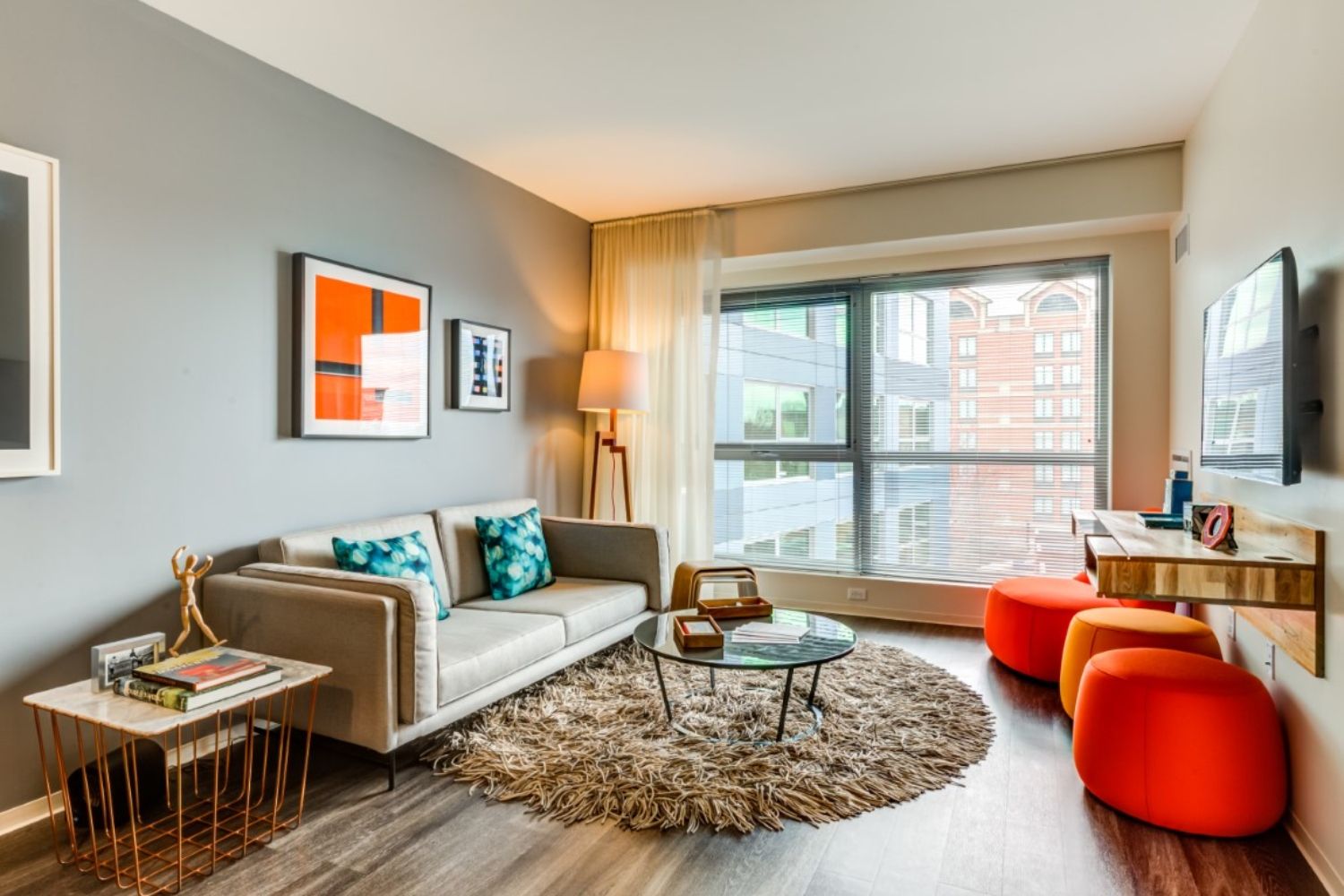 Modern living room with a gray wall, sofa, orange accents, and large window.