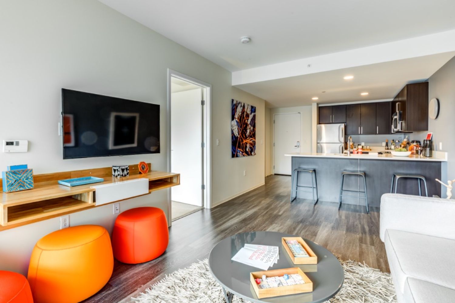 Modern living room with orange stools, a TV, and open kitchen space.