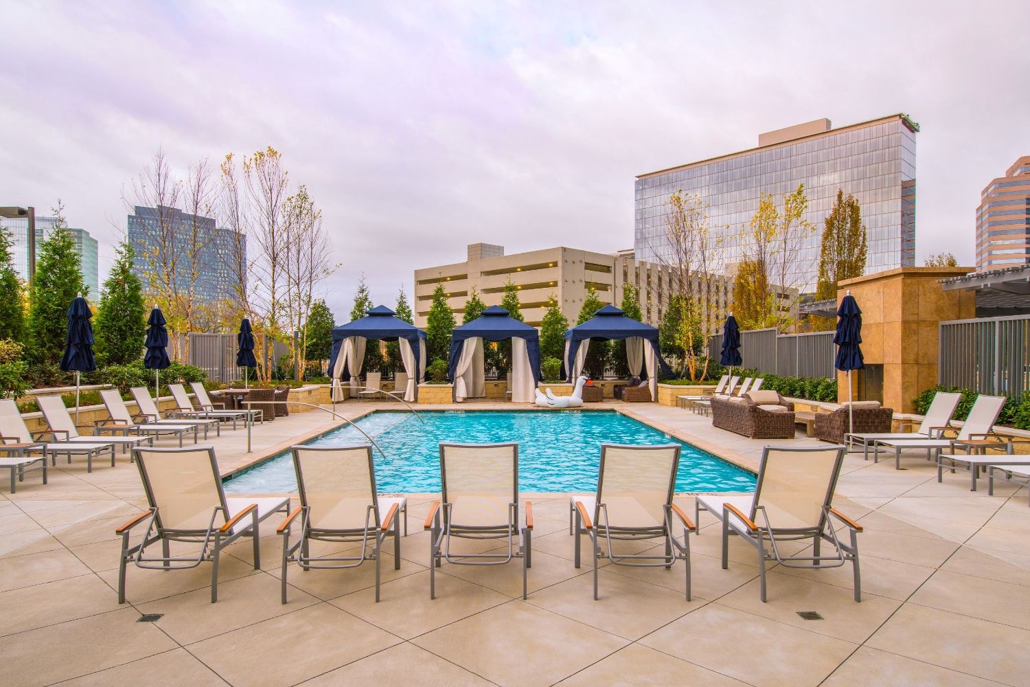 Outdoor swimming pool with lounge chairs and cabanas, surrounded by modern buildings.