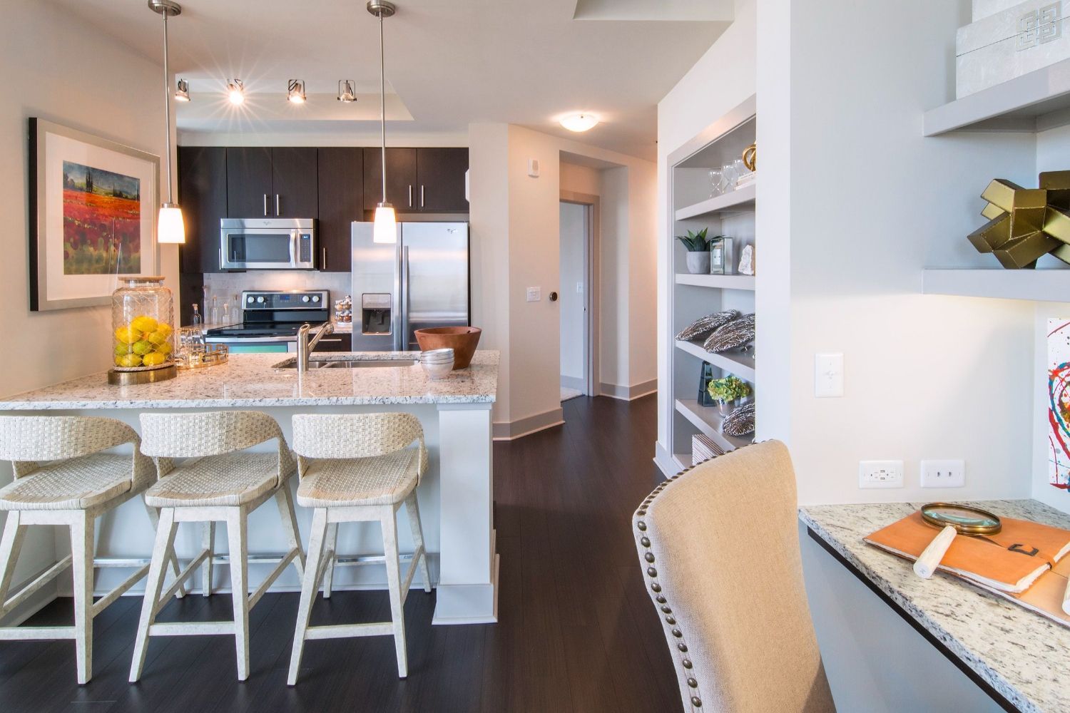 Modern kitchen with bar stools, sleek appliances, and an adjacent hallway.