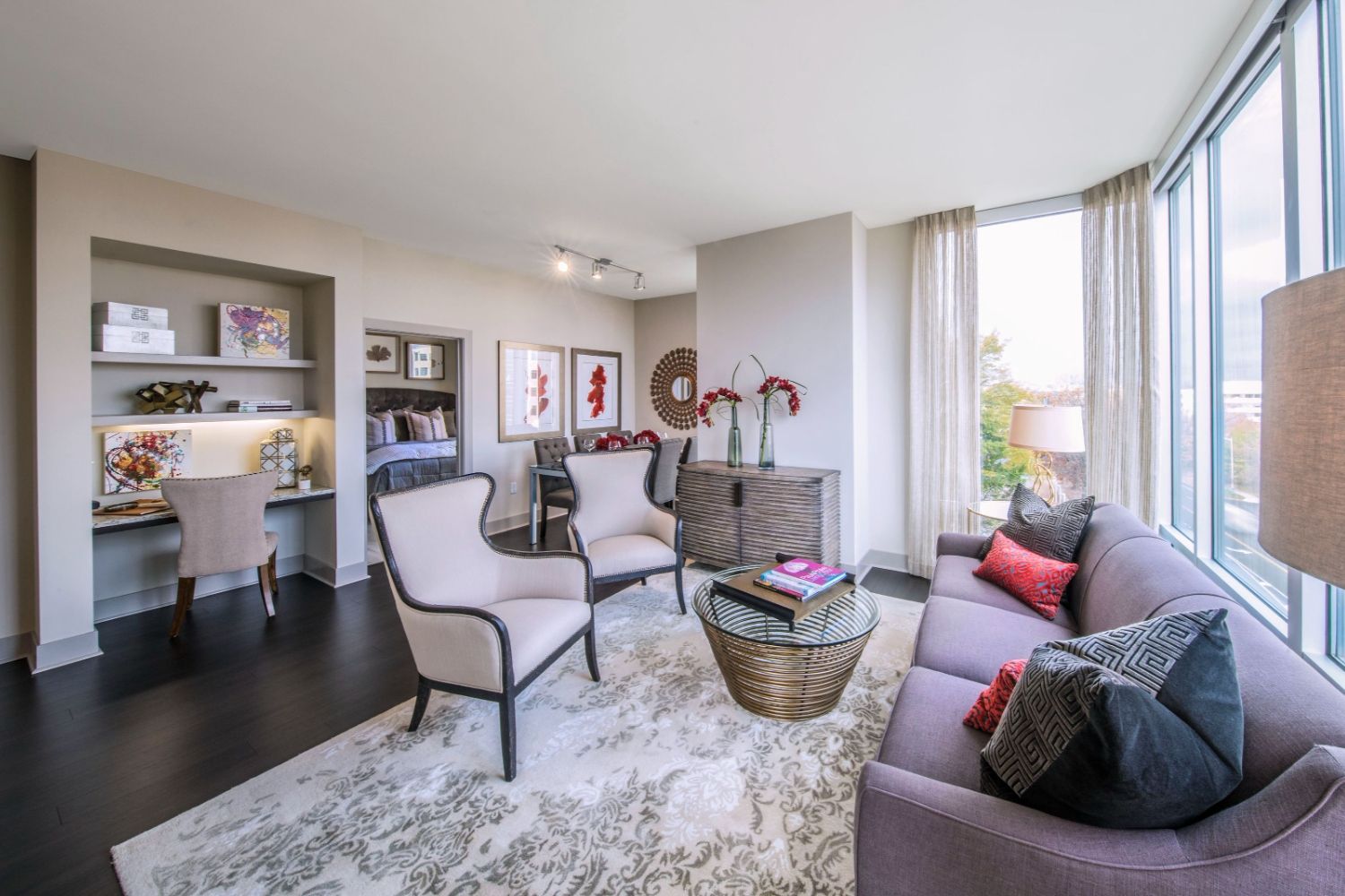 Modern living room with gray furniture, artwork, and large windows letting in natural light.