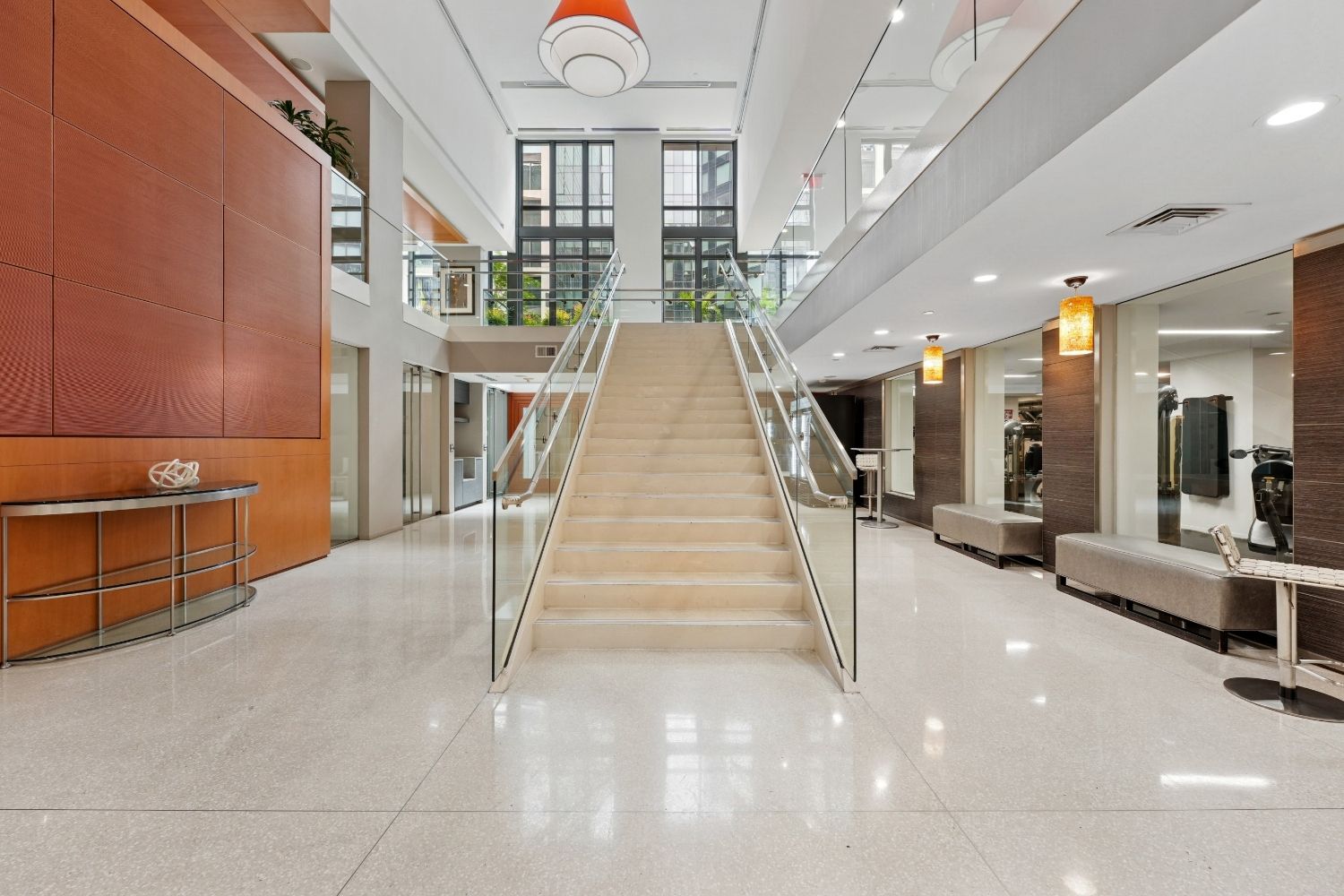 Modern lobby with a staircase, seating areas, and large windows, featuring a warm color palette.