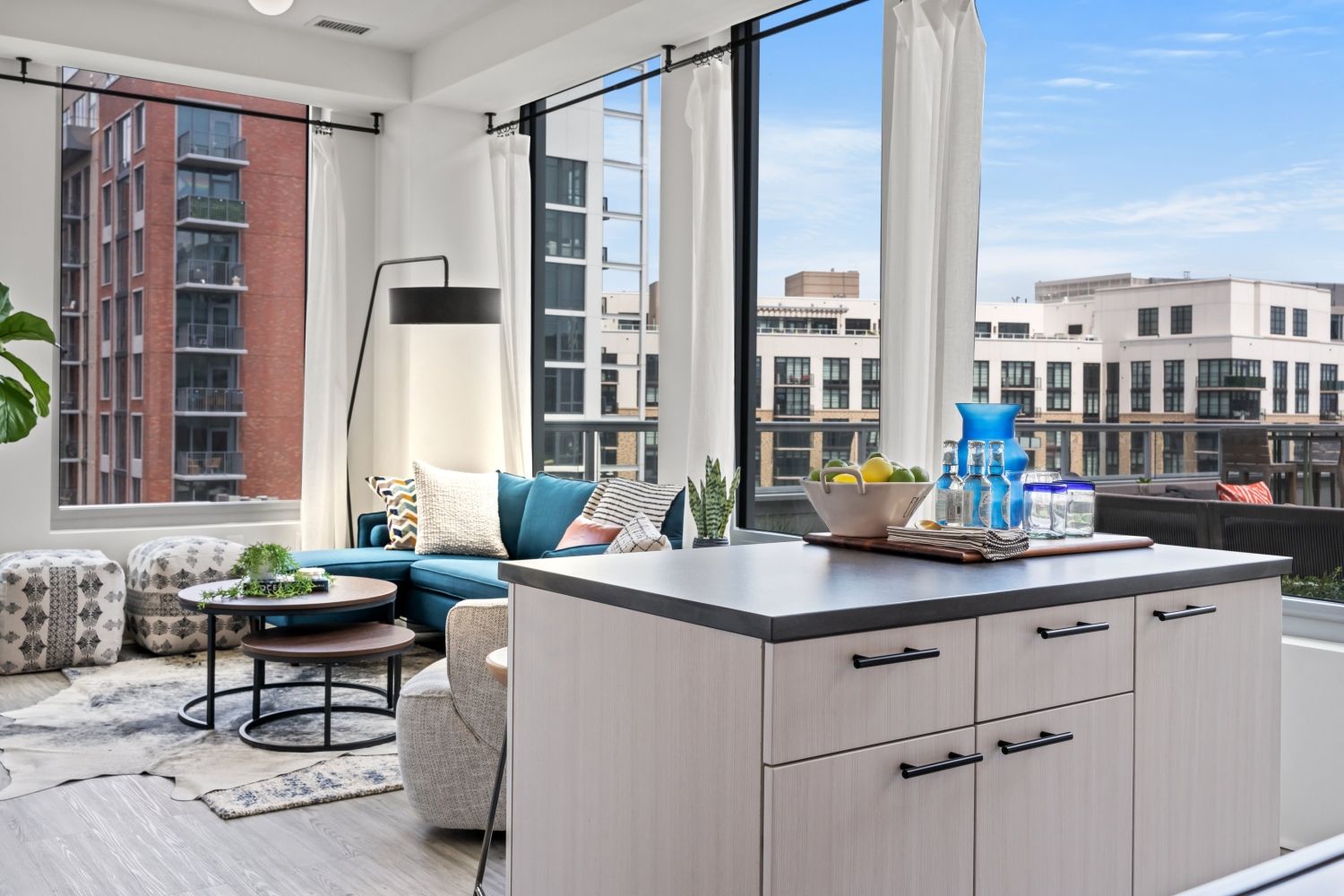 Modern living room with a sofa, coffee table, and large windows showing an urban view.