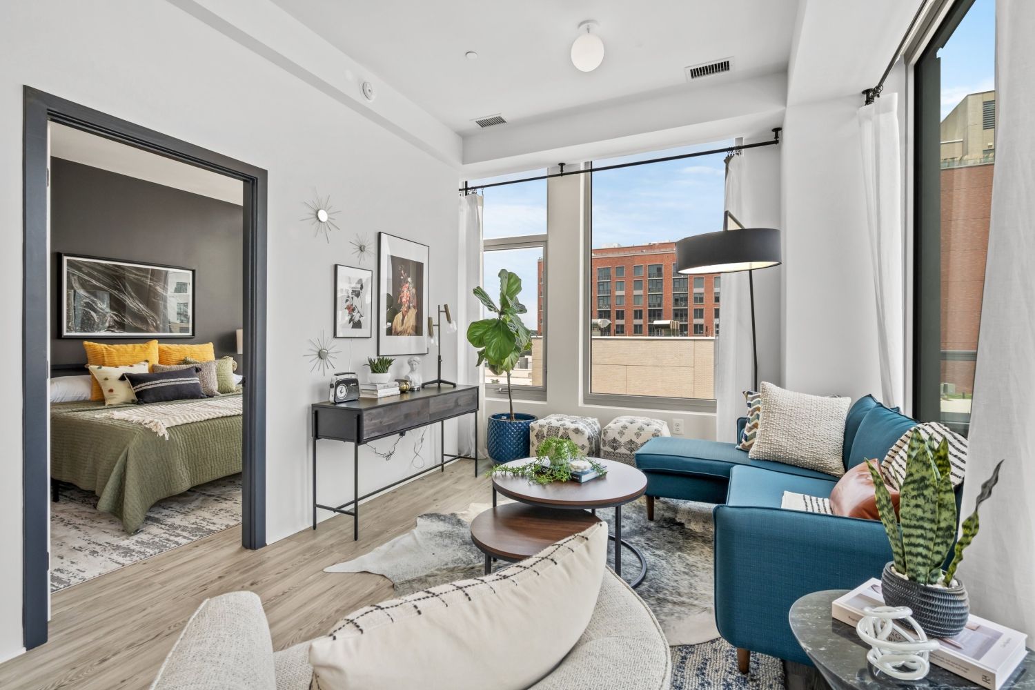 Modern living room with a blue couch, plants, and large windows overlooking a cityscape.