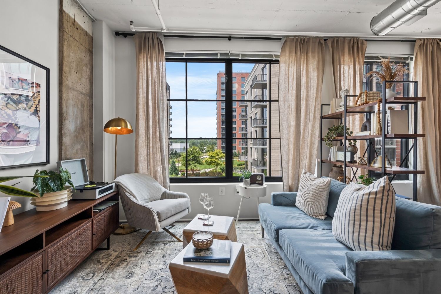 A cozy living room with a view, featuring a sofa, armchair, and plants by large windows.