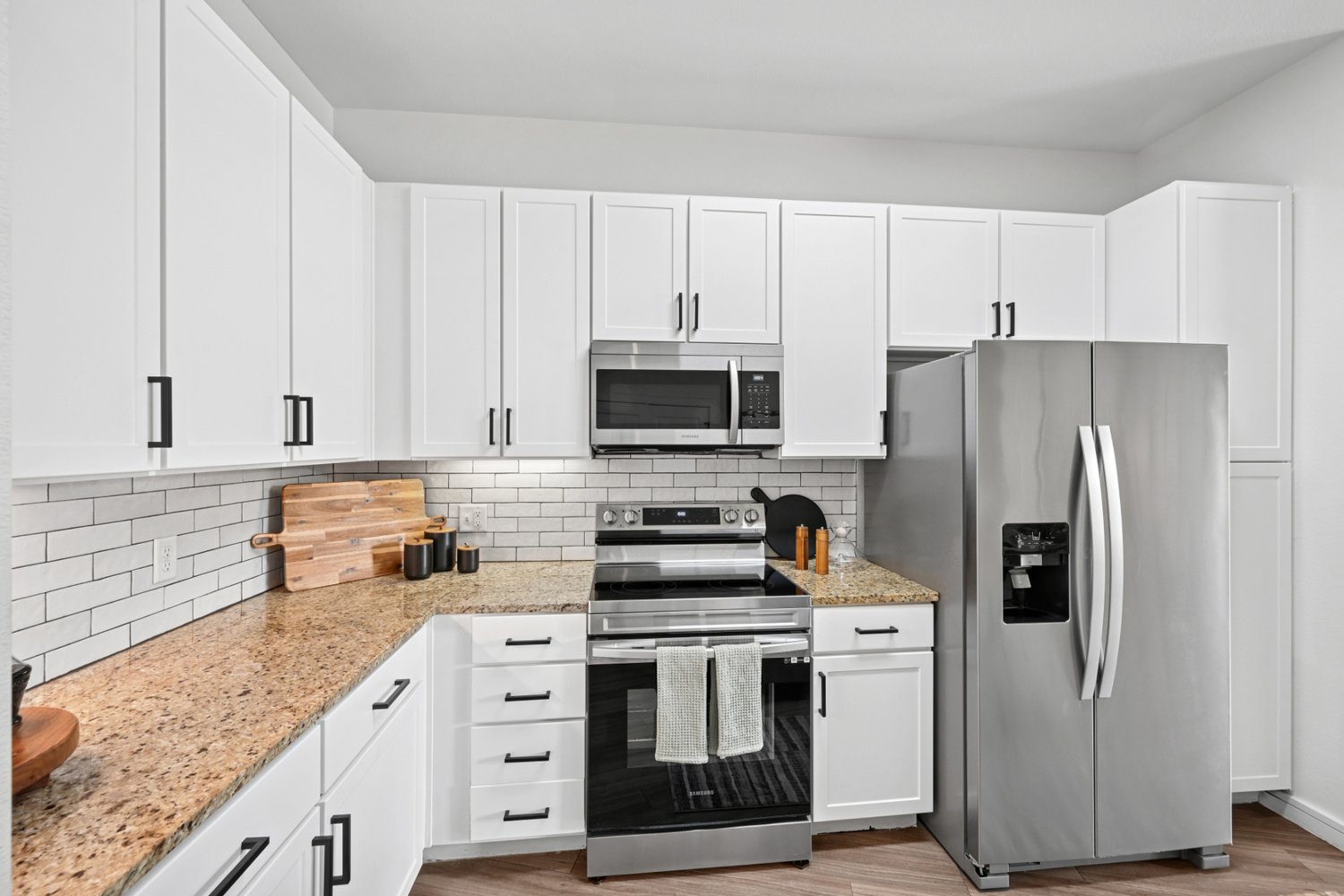 An Aera RiNo apartment kitchen in Denver has white cabinets, granite countertops, and stainless steel appliances.