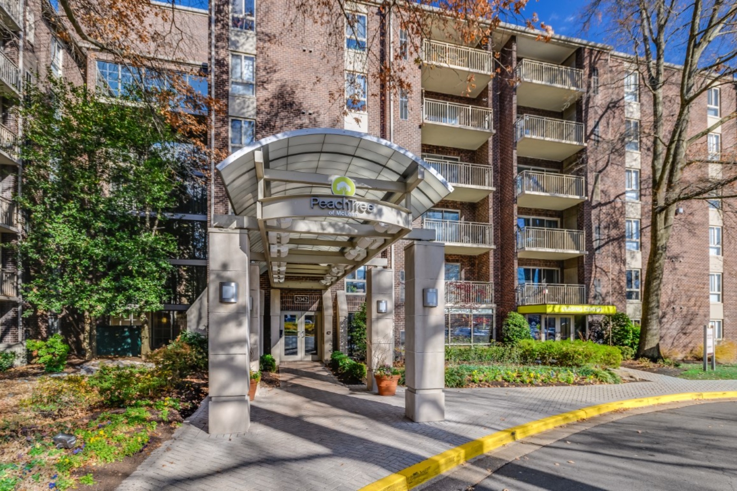 Modern apartment building entrance with a glass canopy and surrounding greenery.