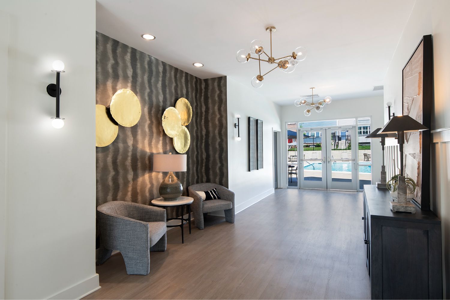 Clubhouse interior at The Villas at Patapsco Glen in Baltimore, MD, with lounge chairs, side tables, wall art, wood-style flooring, and glass doors ov