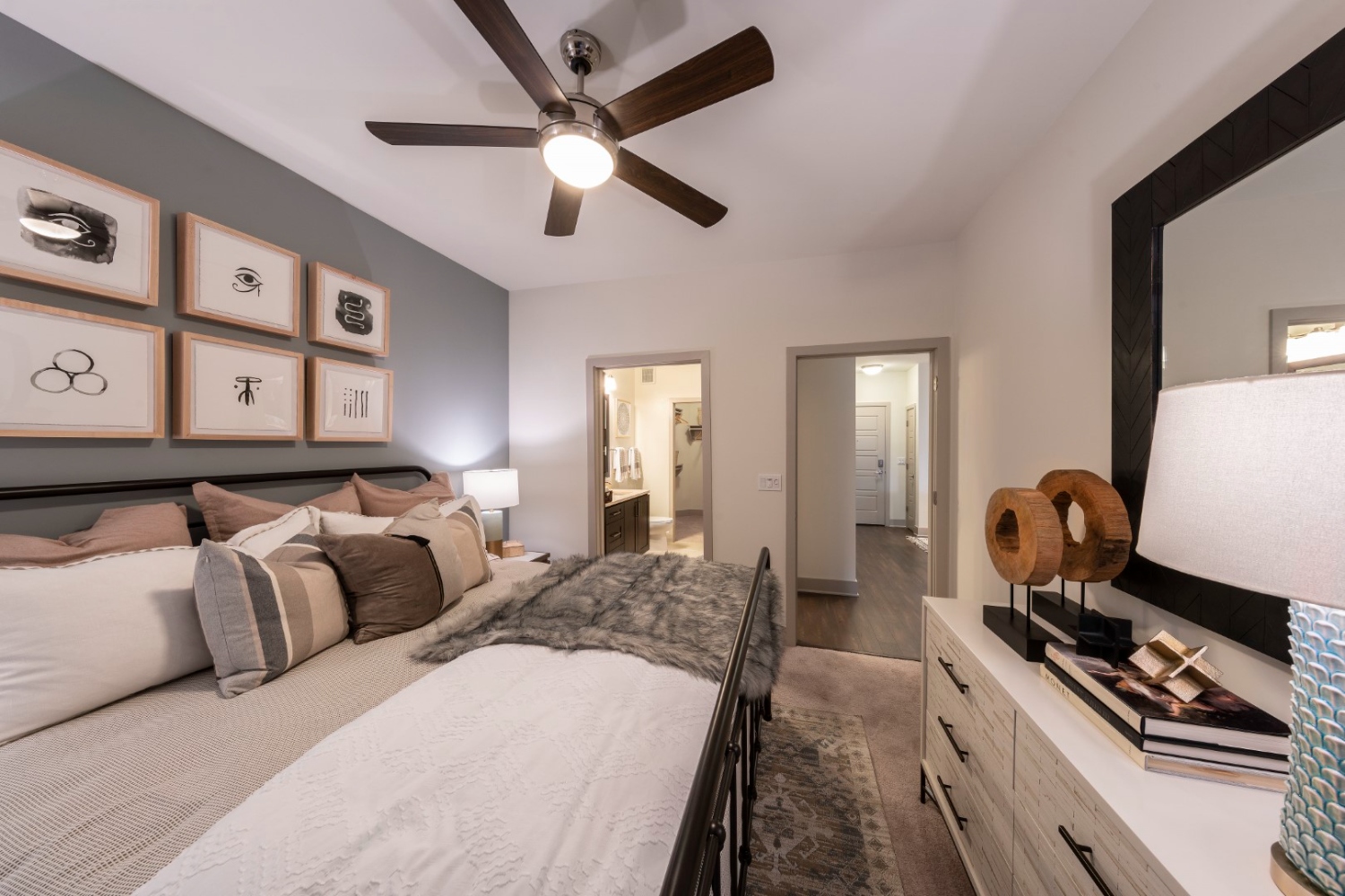 A softly lit bedroom featuring a bed, dresser, and wall art.