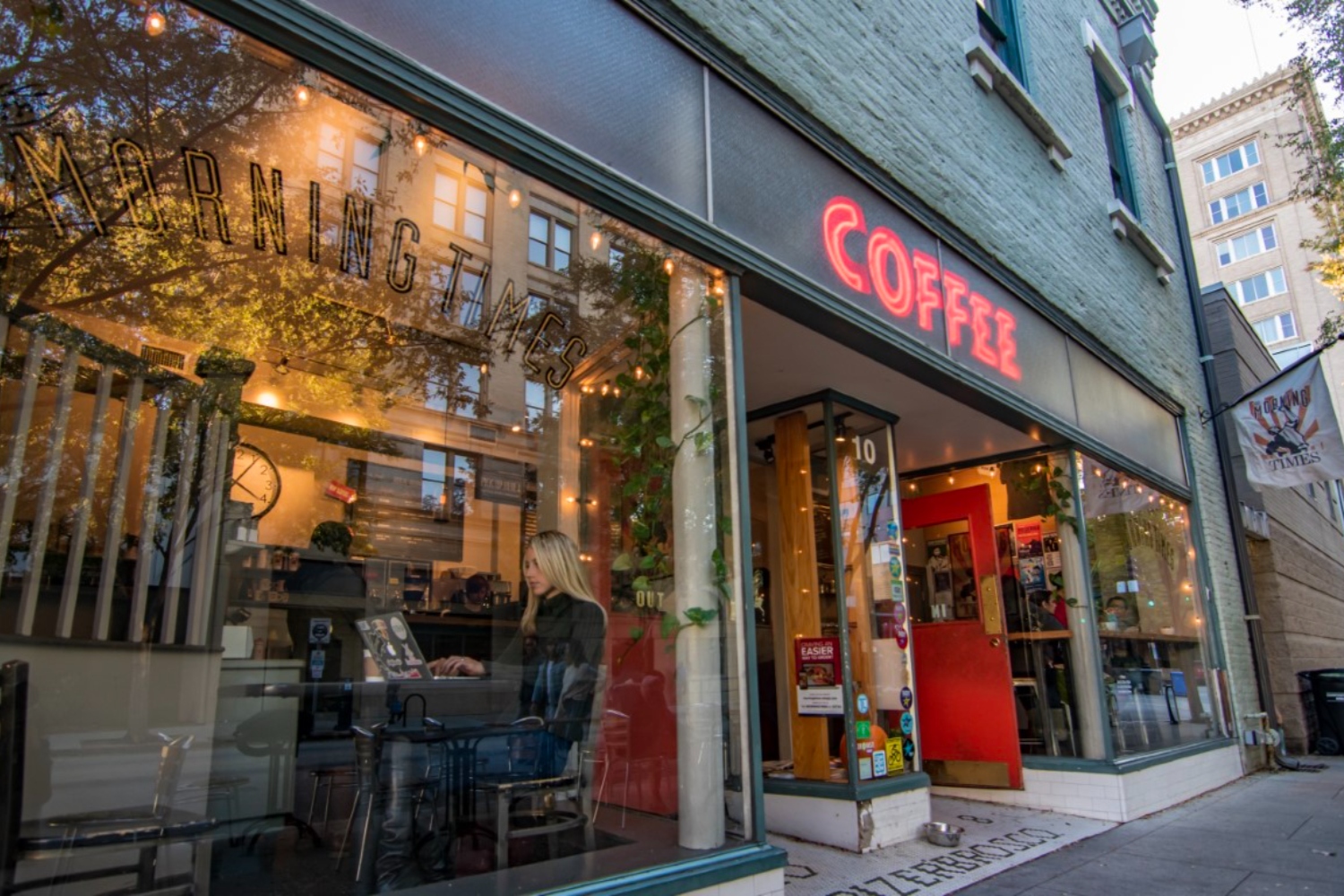 Coffee shop window with warm lighting and greenery, showcasing a cozy interior.