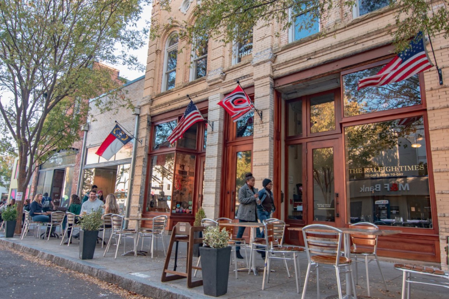 Historic building with outdoor seating and U.S. flags along a tree-lined street.