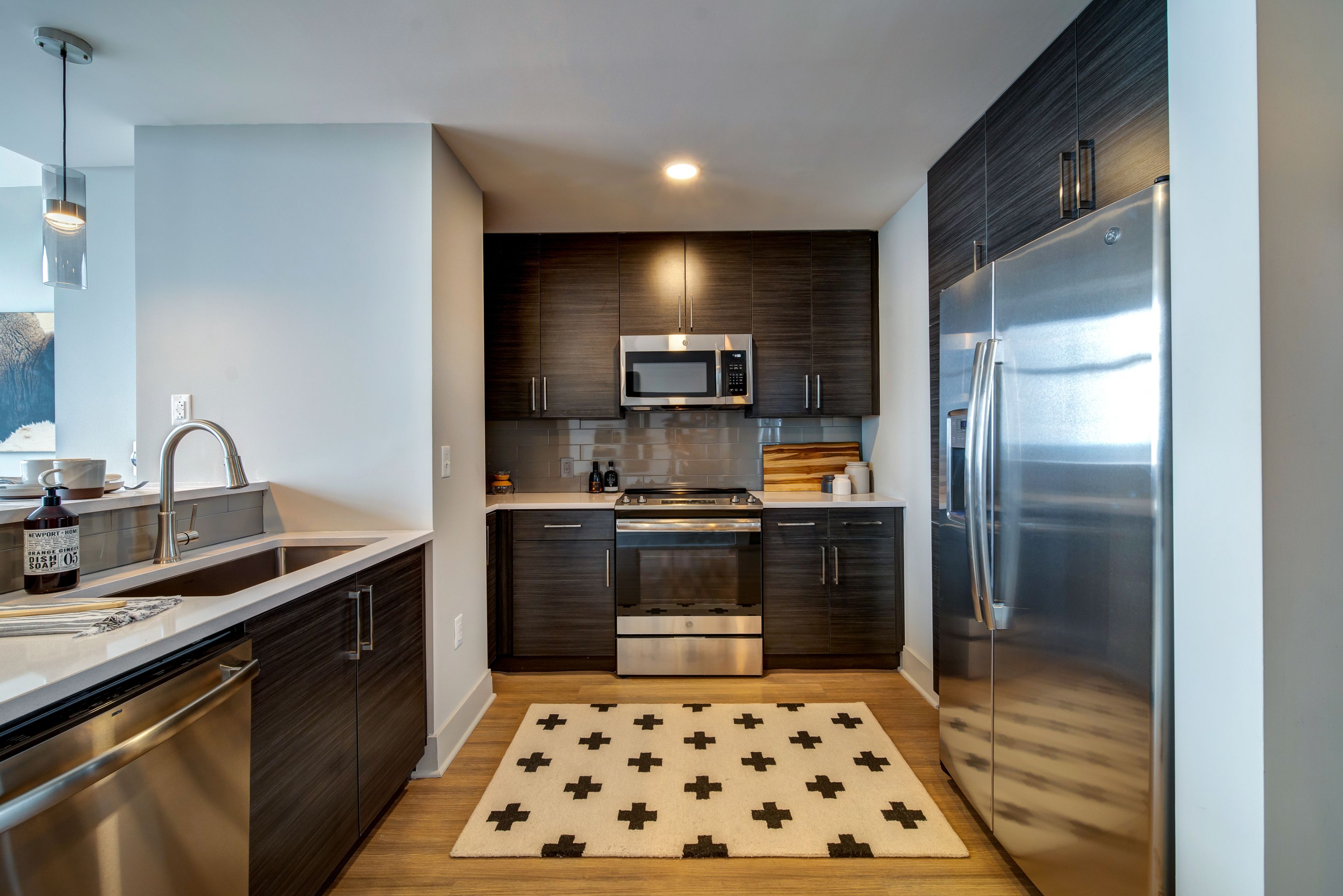 Modern kitchen with dark cabinets, stainless steel appliances, and a patterned rug.