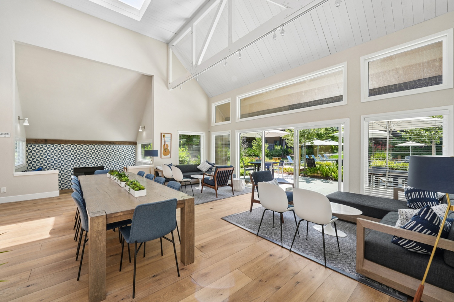 Clubhouse dining area with long wood table, blue accent mural wall, and adjacent kitchen