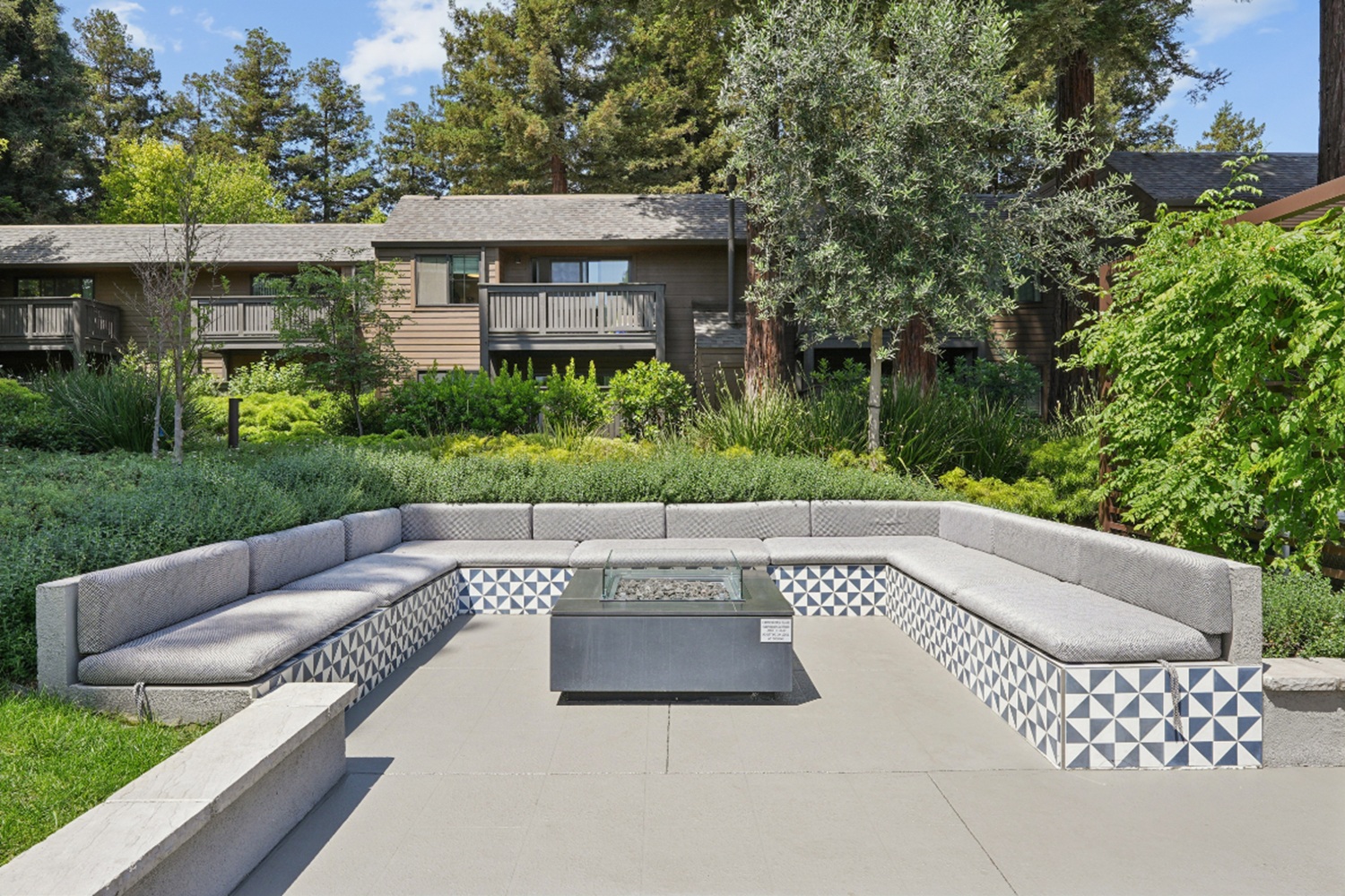 Outdoor fire pit with built-in seating and surrounding greenery at Old Orchard Apartments
