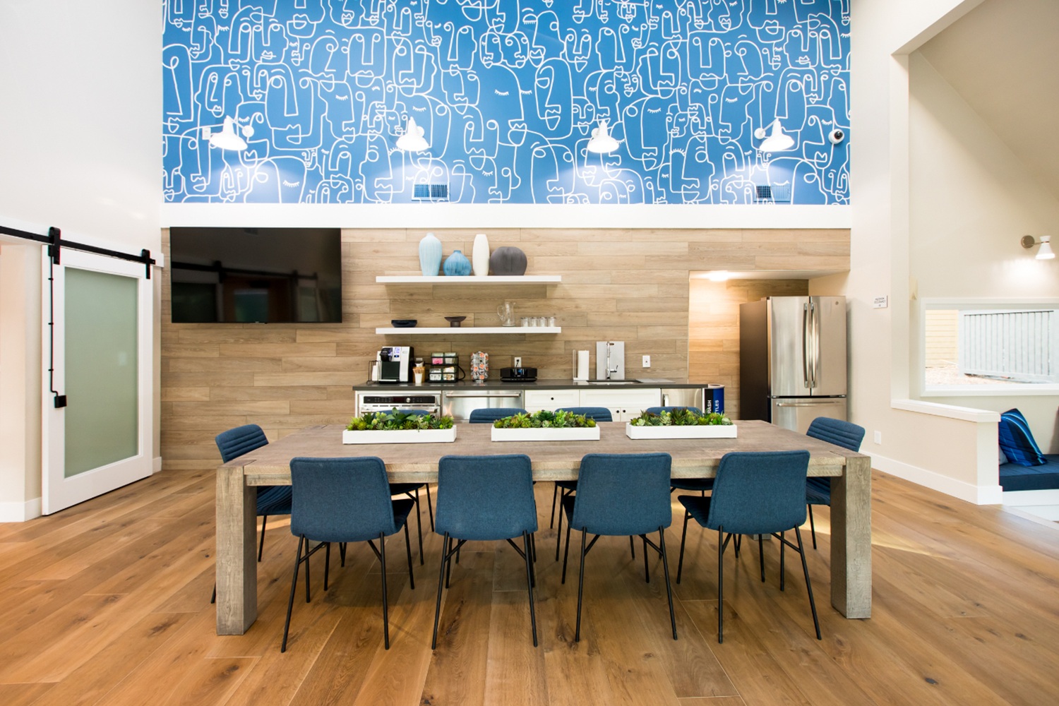 Clubhouse kitchen with stainless steel appliances, blue accent wall, and large communal dining table