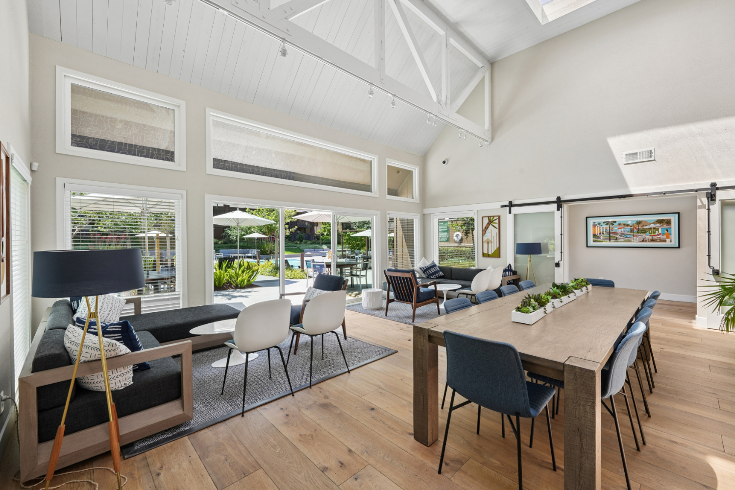 Clubhouse dining area with long wood table, blue accent mural wall, and adjacent kitchen