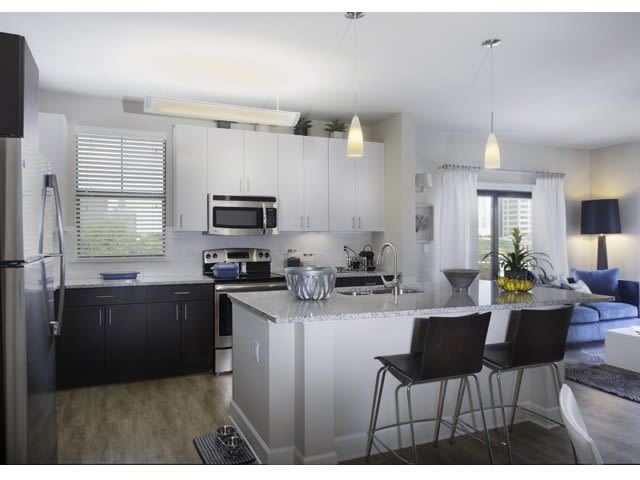 Modern kitchen with island bar, stainless steel appliances, and light cabinetry.