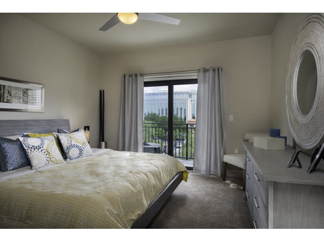 Modern bedroom with a queen bed, dresser, and large window overlooking greenery.