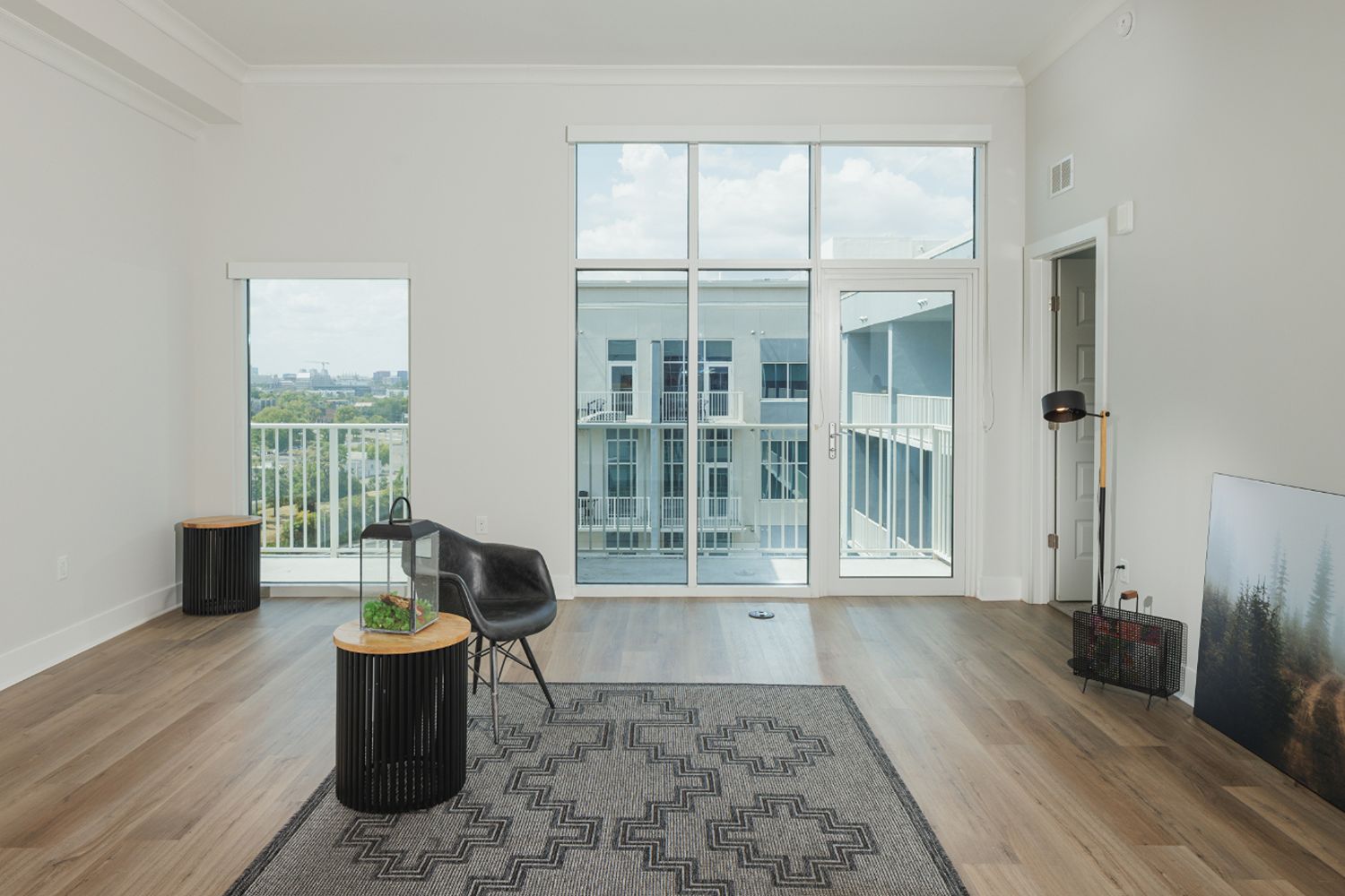 Living room with tall windows, balcony doors, wood-look flooring, and a small seating arrangement.