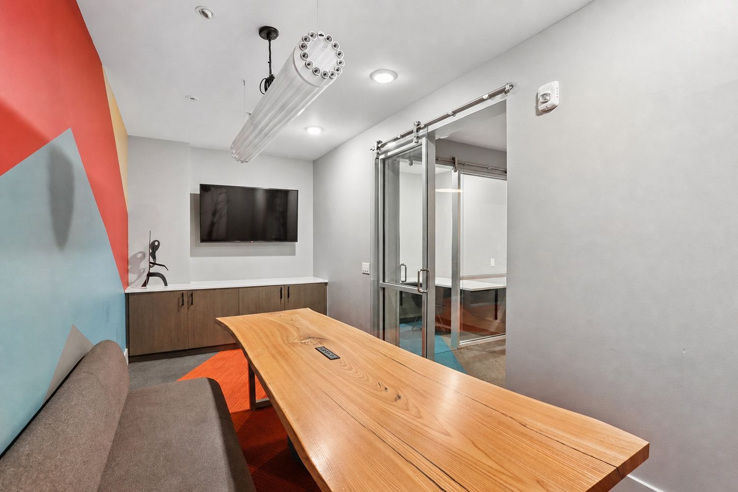 Glass-enclosed conference room with a long wood table, bench seating, and a wall-mounted television at The Hartwell.