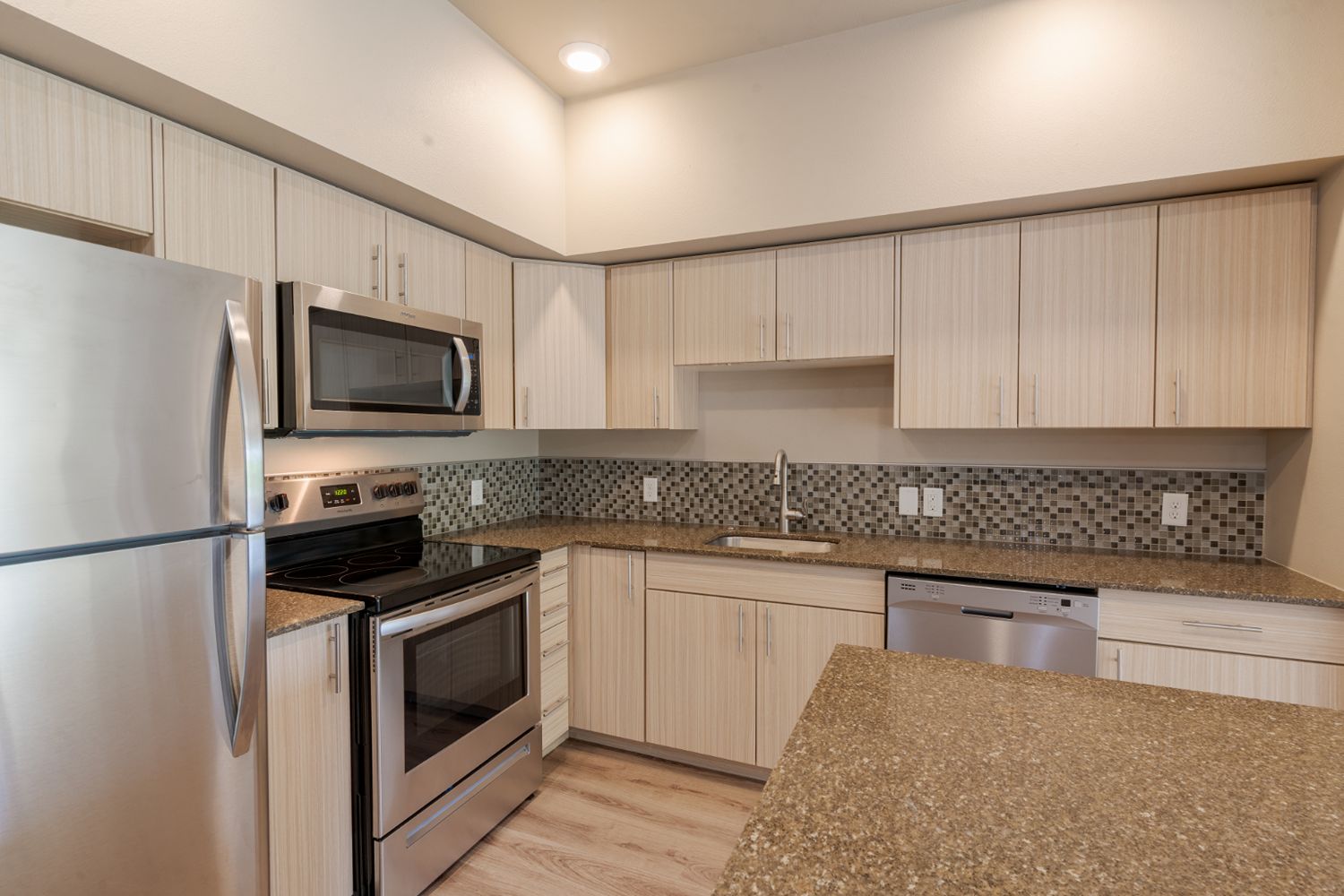 Kitchen with light wood cabinetry, stainless steel appliances, and a mosaic tile backsplash.