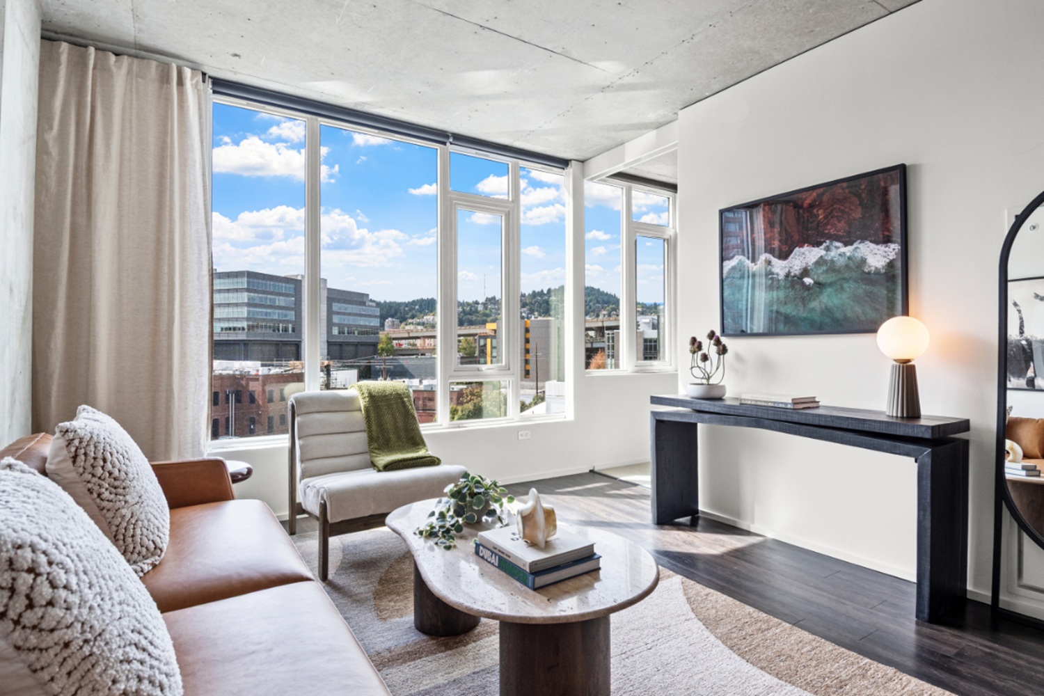 Apartment living room at NV Apartments with oversized windows, modern furniture, and Portland skyline views.