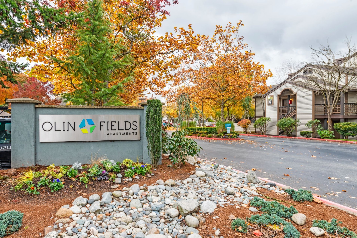 Olin Fields Apartments welcome sign surrounded by autumn foliage.