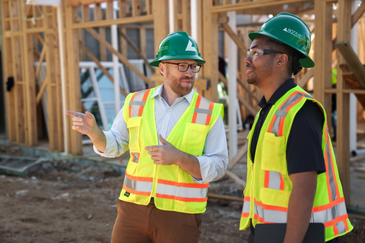 Two construction workers in safety vests and hard hats discussing on a building site.