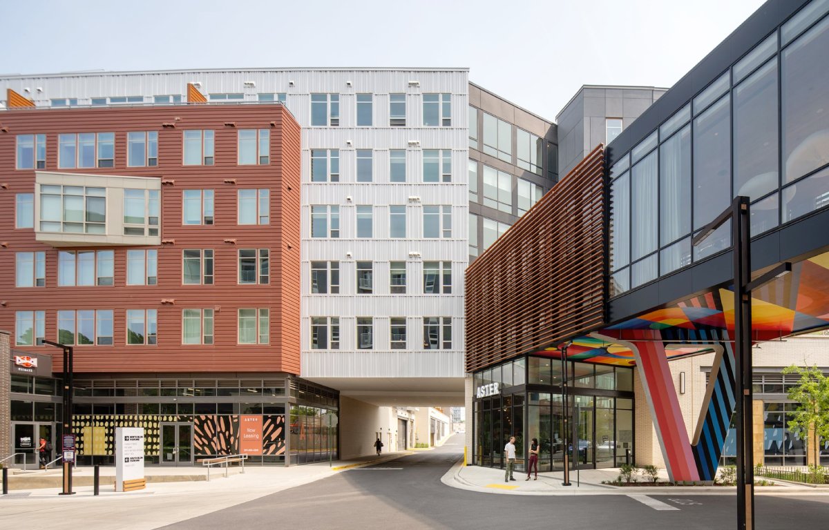 Modern urban buildings with varied facades and an open walkway between them.