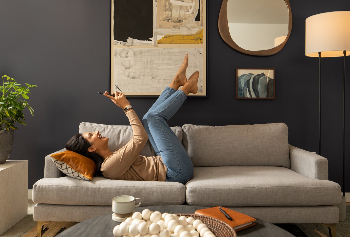 Woman reclining on a gray couch with legs up, in a stylish living room.