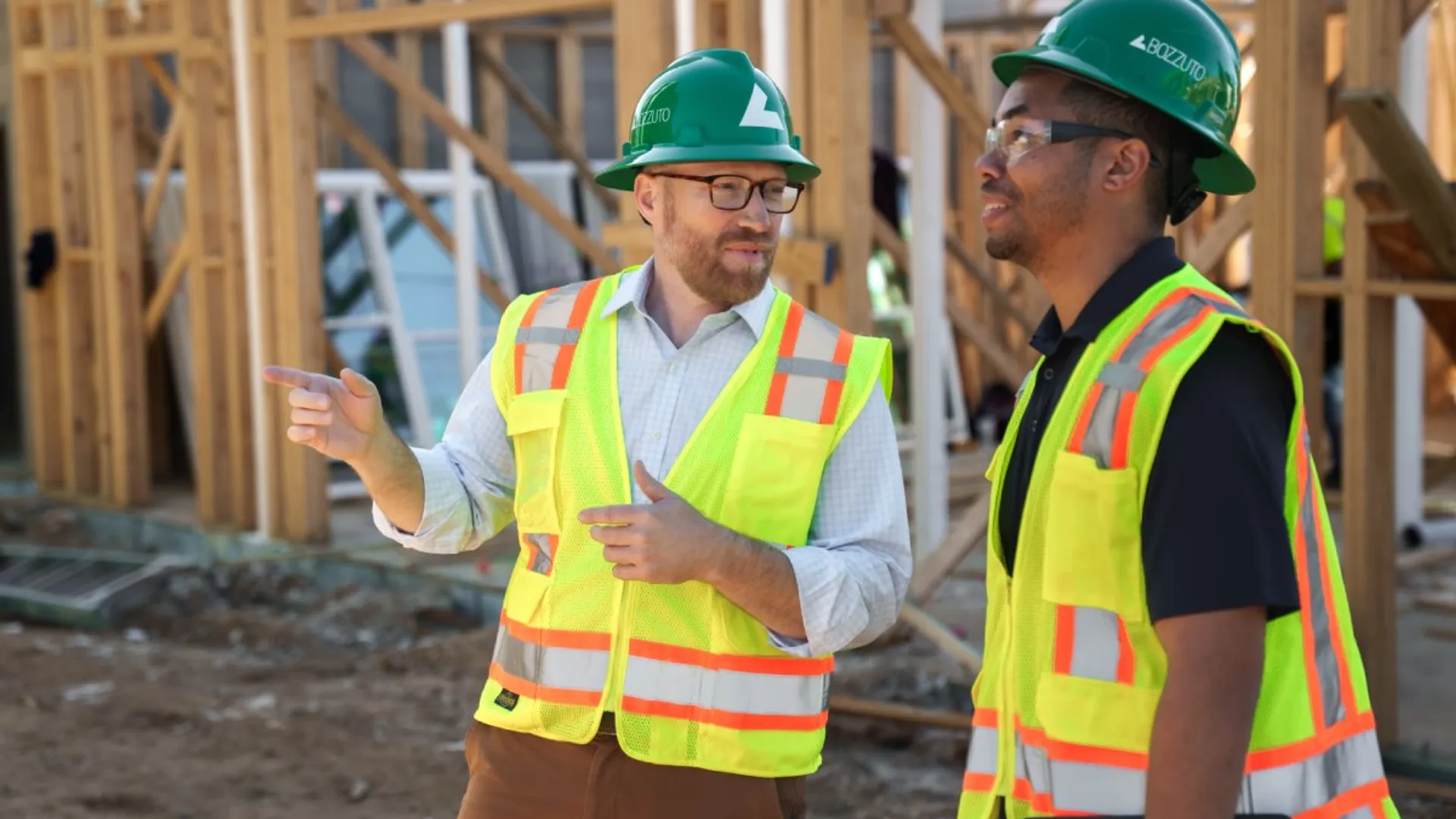 Two construction workers in safety vests and hard hats discussing on a building site.