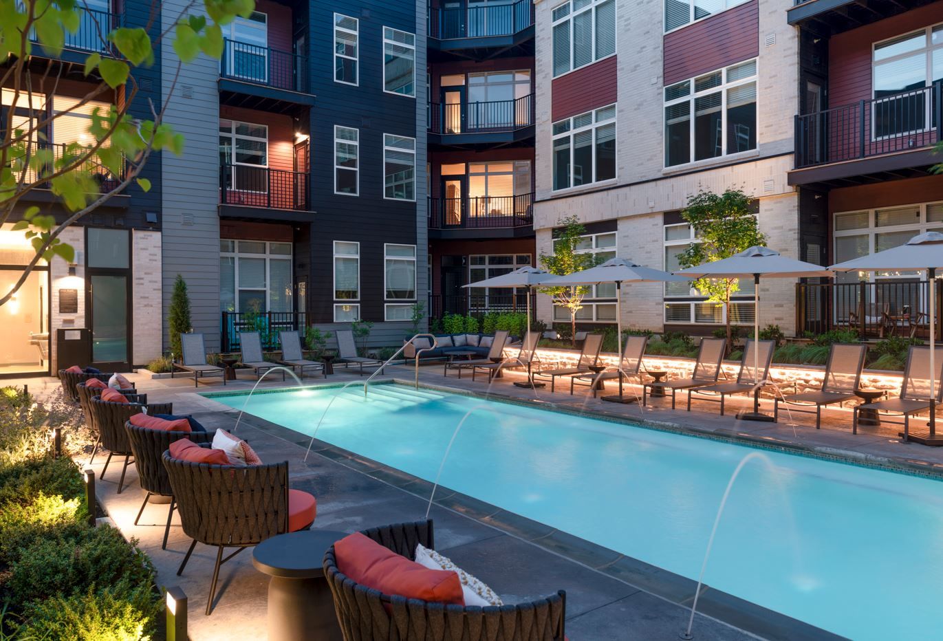 Modern apartment complex pool area with lounge chairs and umbrellas.