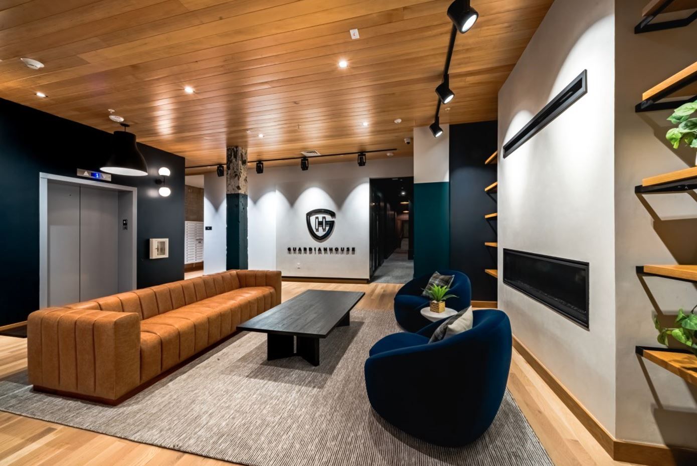 Modern lobby with a brown sofa, blue chairs, wooden accents, and decorative shelves.