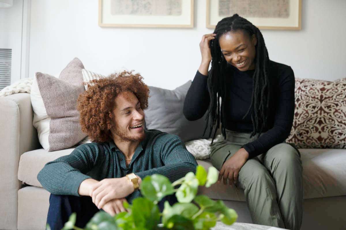 A smiling couple sitting together on a couch, sharing a light moment indoors.