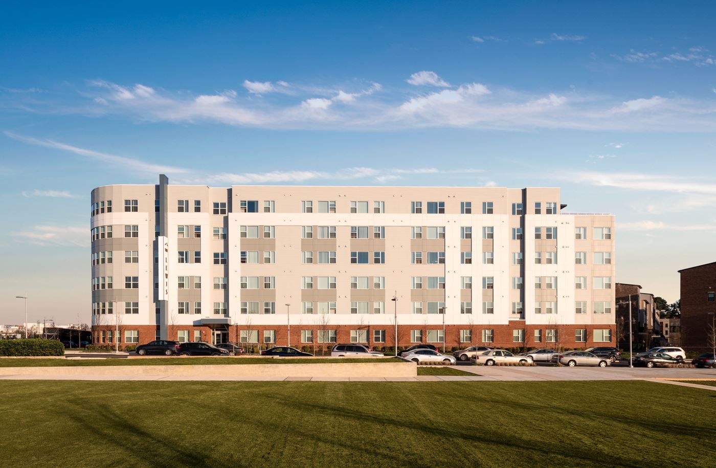 Modern multi-story building with a grassy foreground under a clear blue sky.
