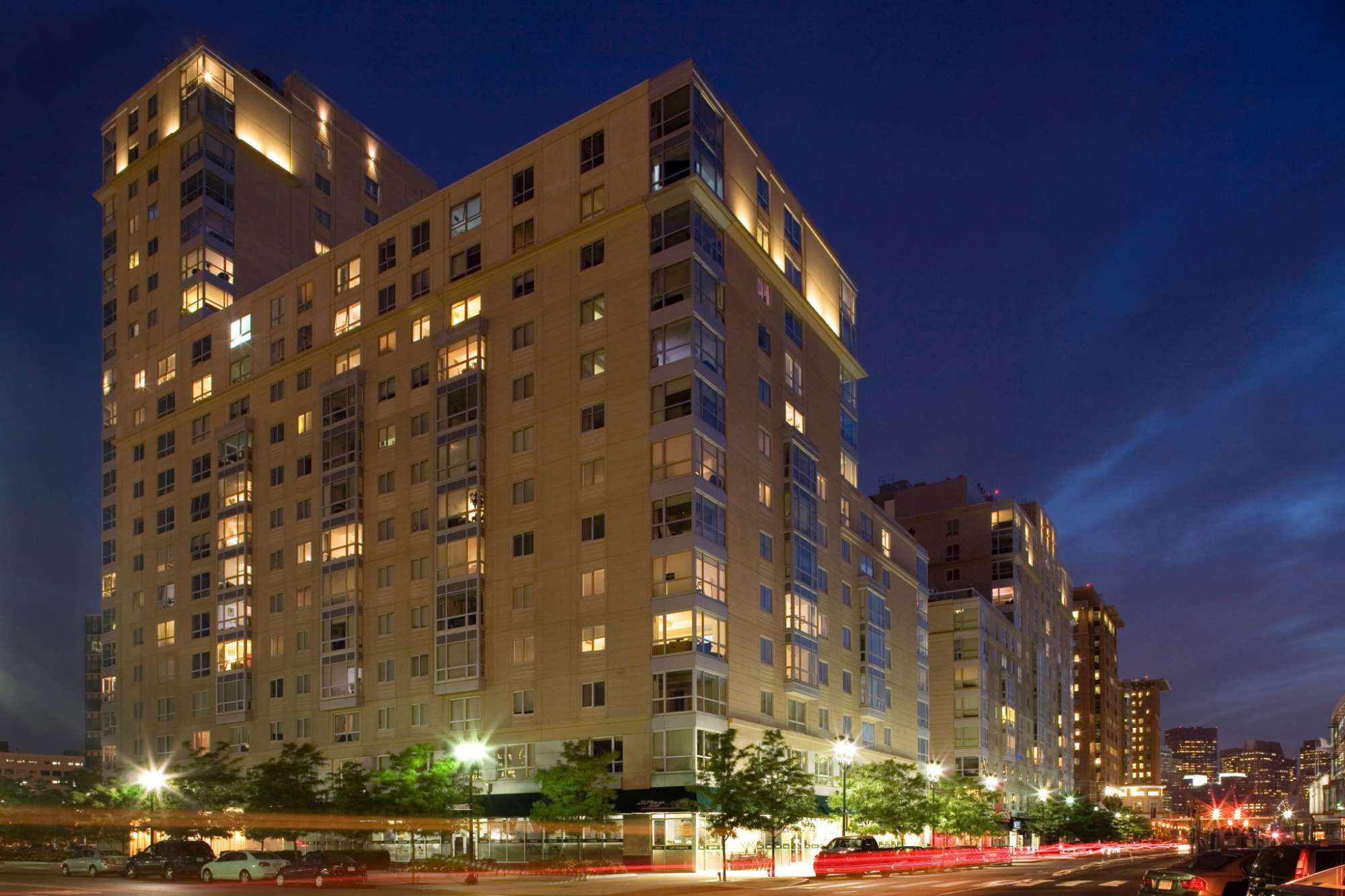 Modern apartment building illuminated at night with a city skyline in the background.