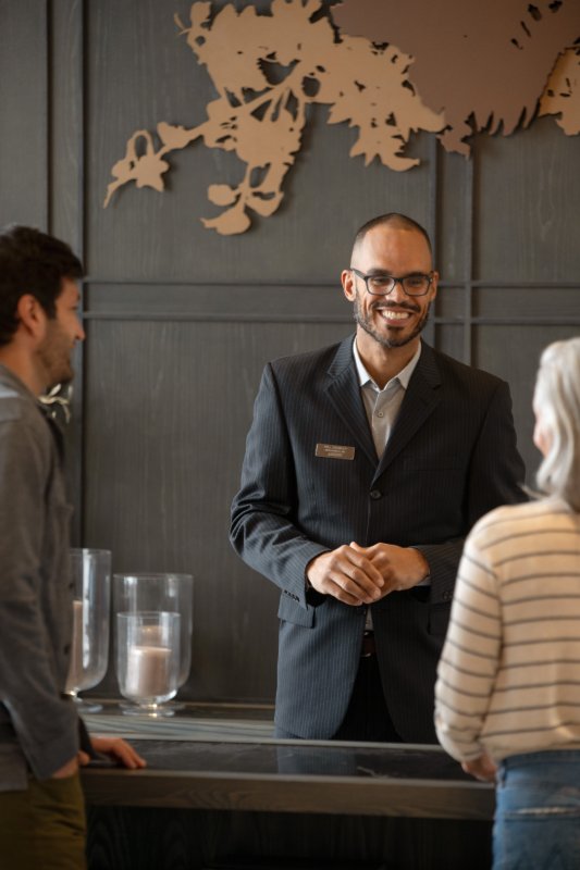 A smiling receptionist assisting two visitors at a front desk.