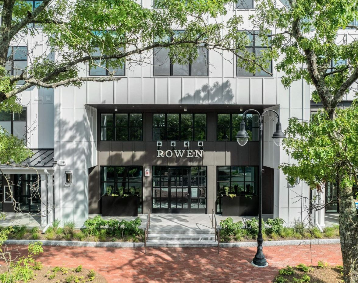 Modern building entrance with "ROWE" sign and large windows, surrounded by trees.