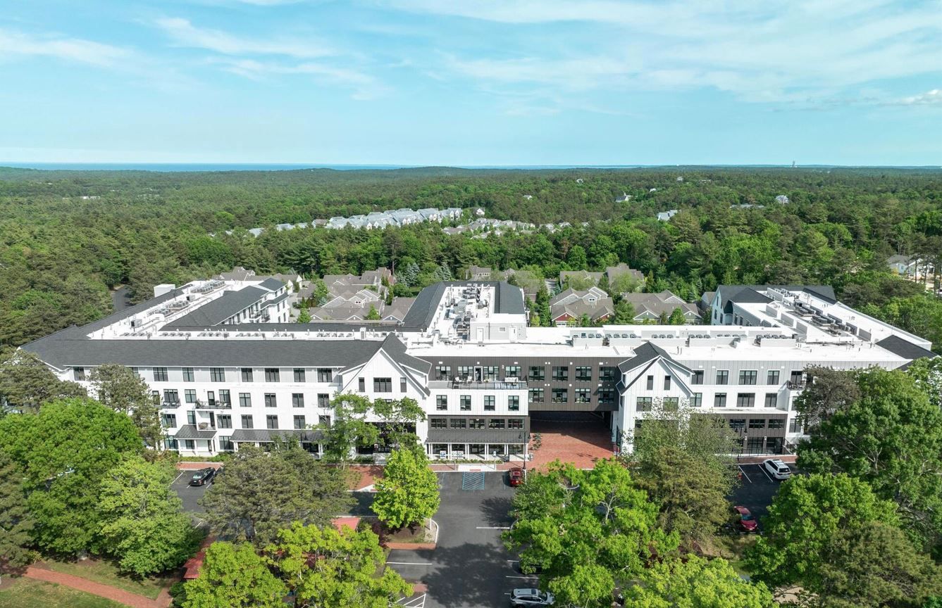Aerial view of a white multi-story building surrounded by trees.