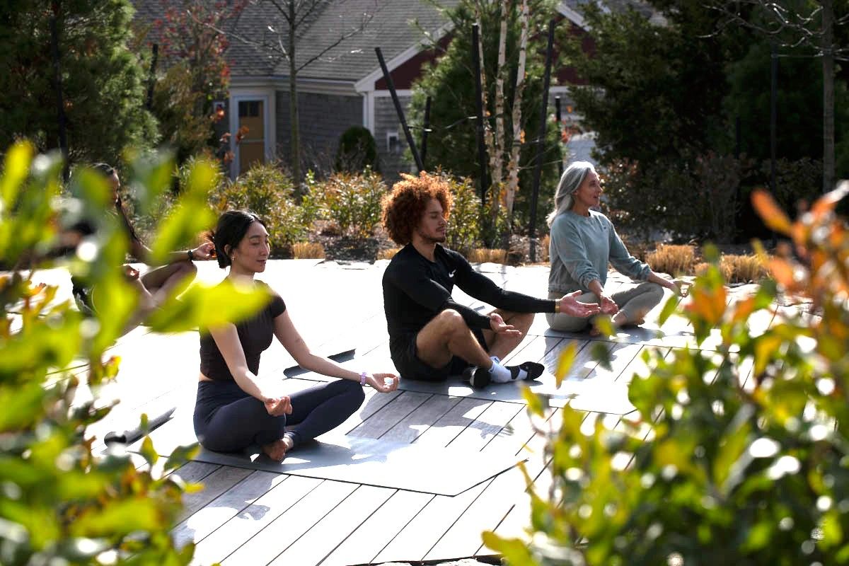 Three people meditating outdoors amidst greenery, embodying a sense of peace.